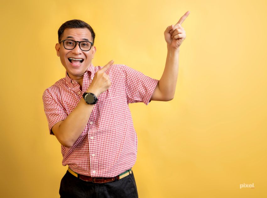 Man with eyeglasses and a shirt pointing at something on a colored background